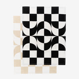 Two ufolded dishtowels with the same pattern, one in a beige-and-white colorway, the other black-and-white. Unfolded, the pattern is a 6x8 checker pattern, the middle 4 rows fragment into half-moon shapes.