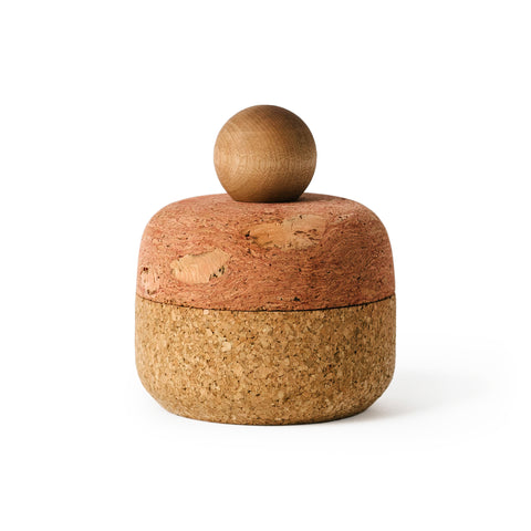 Squircle shaped container with equally proportioned pink cork lid and brown cork bottom with a sphere-shaped maple wood handle, shot on a white background.
