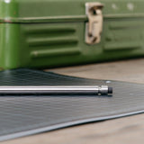 Detail image of the back end of the Handmade Stainless Steel Pencil, lying on a cutting mat with a green, out of focus toolbox in the background.
