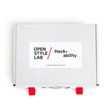 A design kit packaged in a white rectangular box that features two bright red tabs at the front of the box for opening and closing. A white sticker is placed at the center of the box cover and features the name of the organization as well as the kit name in bold black text.  