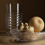 Glass vase and bowl made up of bulbous ridges. Bowl is oblong and holds a butternut squash and fresh ginger. Vase holds a single stem.