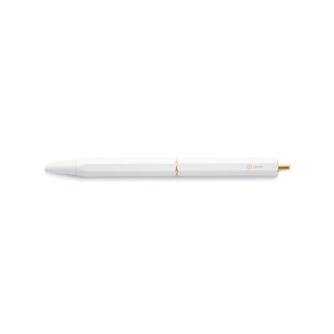 The White Brassing Portable Ball Point Pen has flat sides for grip, a brass-colored scalloped center seam, a small, brass-colored, ystudio logo, and a narrow, brass end.